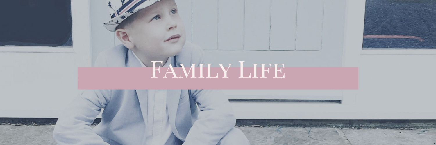Neurodiverse family life - Image show young boy of approx. 7 years of age sitting on the front step outside the front door. He is wearing a pale blue suit, white shirt, sneakers and a panama hat
